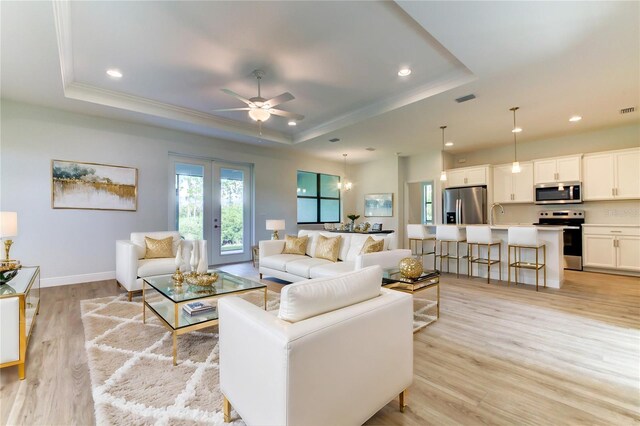 living room with light hardwood / wood-style flooring, a tray ceiling, and ceiling fan