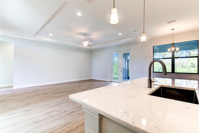 kitchen with ceiling fan with notable chandelier, light wood-type flooring, light stone counters, and hanging light fixtures