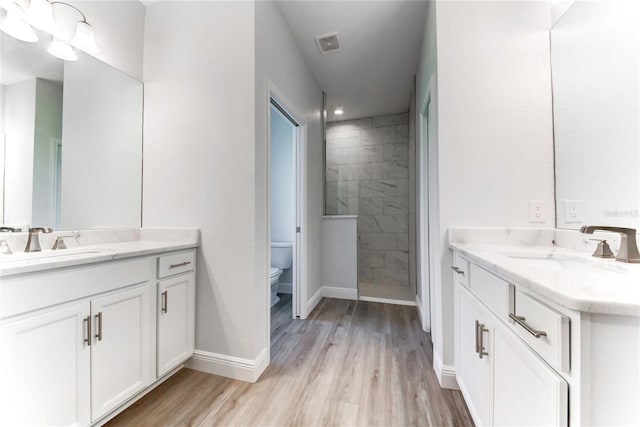 bathroom featuring vanity, hardwood / wood-style floors, toilet, and tiled shower