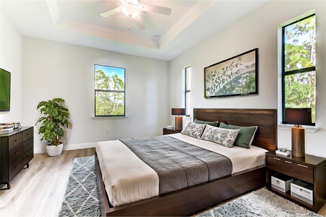 bedroom featuring a raised ceiling, multiple windows, and light hardwood / wood-style flooring