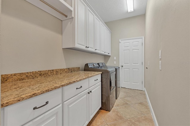 laundry room with cabinets, light tile patterned flooring, washer and dryer, and a textured ceiling