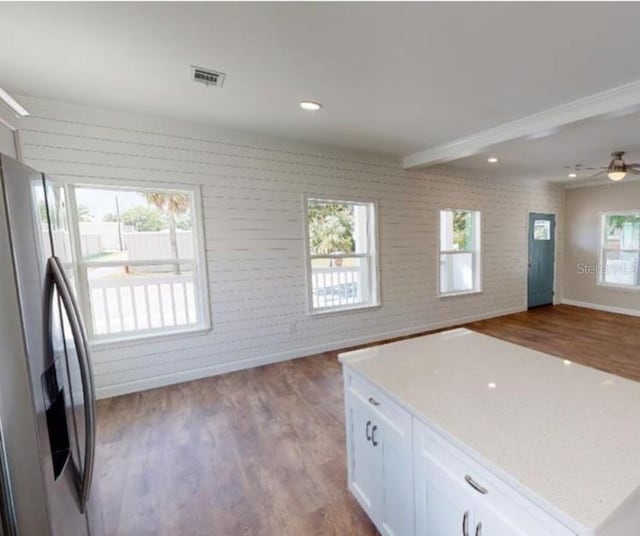 kitchen featuring stainless steel fridge, dark wood-style flooring, brick wall, visible vents, and white cabinets