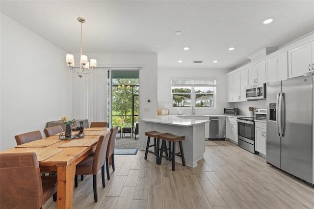 kitchen featuring pendant lighting, white cabinetry, appliances with stainless steel finishes, a kitchen breakfast bar, and light wood-type flooring