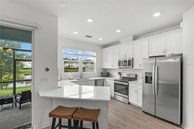 kitchen with sink, kitchen peninsula, white cabinetry, appliances with stainless steel finishes, and light hardwood / wood-style floors