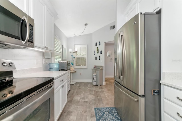 kitchen with pendant lighting, light wood-type flooring, white cabinets, stainless steel appliances, and backsplash