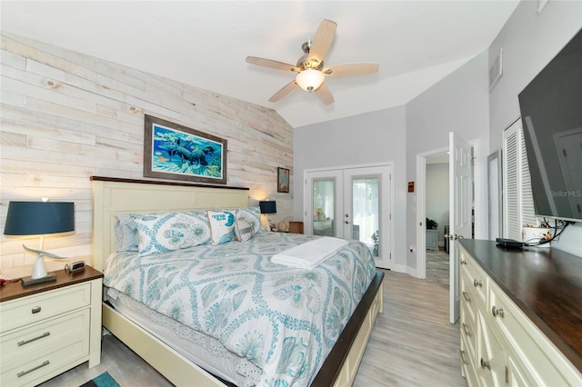 bedroom with lofted ceiling, ceiling fan, french doors, light hardwood / wood-style flooring, and wooden walls