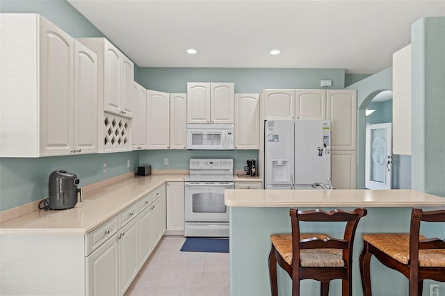 kitchen with a kitchen breakfast bar, white cabinets, white appliances, light tile patterned floors, and sink