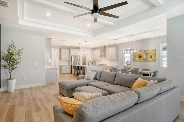 living room featuring ceiling fan, a tray ceiling, light wood-type flooring, and sink