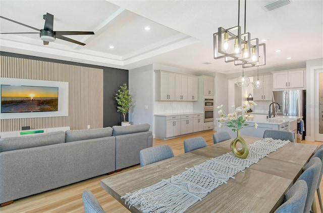 dining space with ceiling fan, sink, a tray ceiling, and light hardwood / wood-style floors