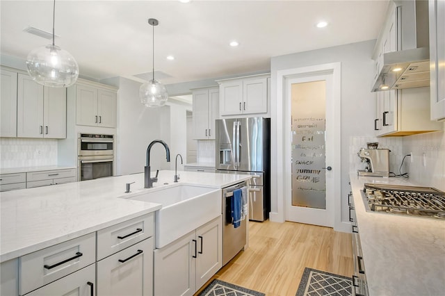 kitchen featuring decorative backsplash, light hardwood / wood-style floors, pendant lighting, stainless steel appliances, and sink