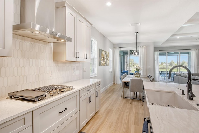 kitchen featuring white cabinetry, decorative light fixtures, wall chimney range hood, and sink