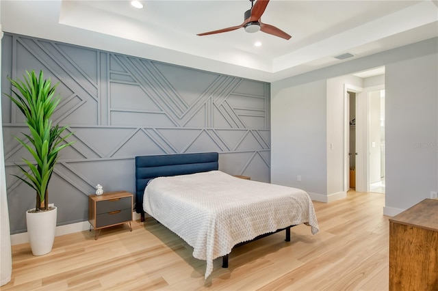 bedroom featuring light hardwood / wood-style floors, a tray ceiling, and ceiling fan