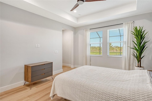 bedroom featuring light wood-type flooring, a tray ceiling, and ceiling fan