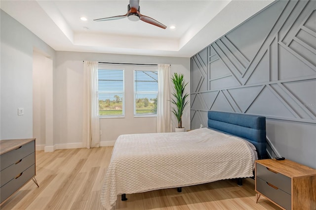 bedroom with light hardwood / wood-style floors, a tray ceiling, and ceiling fan