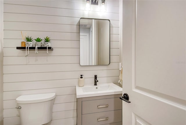 bathroom with wood walls, vanity, and toilet