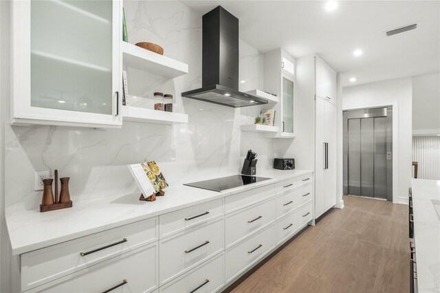 kitchen featuring light stone countertops, black electric stovetop, white cabinetry, and wall chimney range hood