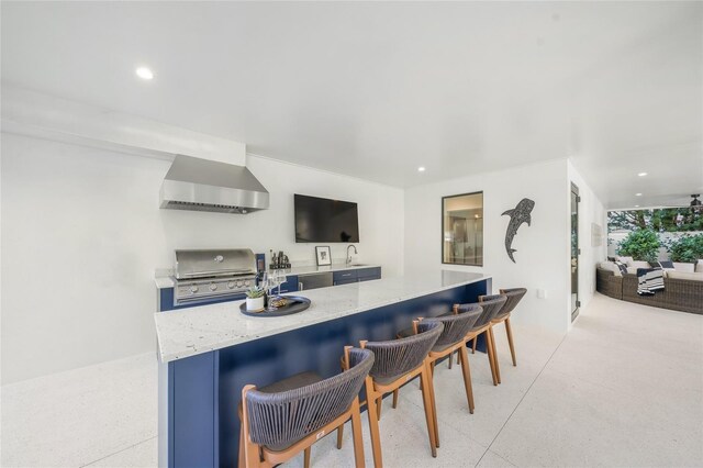 kitchen with a kitchen breakfast bar, sink, light stone counters, and wall chimney range hood