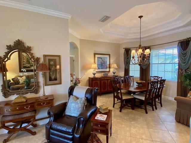 dining room featuring a notable chandelier, a tray ceiling, ornamental molding, and light tile patterned flooring