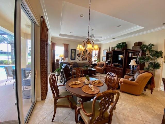 tiled dining space with a raised ceiling, ornamental molding, and a notable chandelier