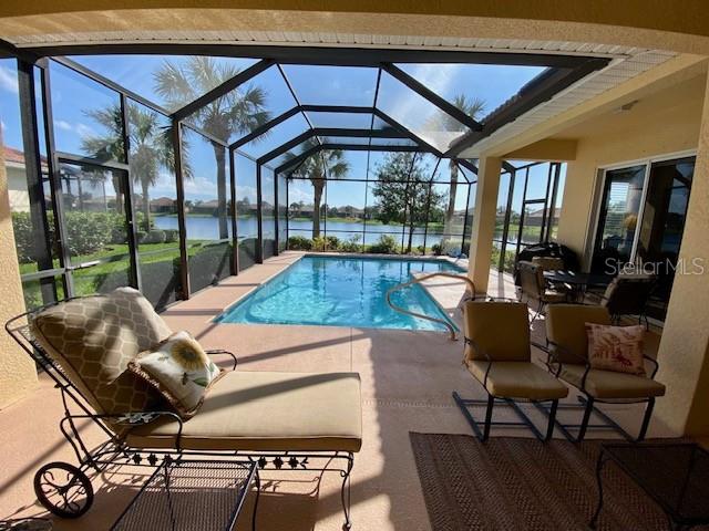 view of pool with a patio, a water view, and glass enclosure