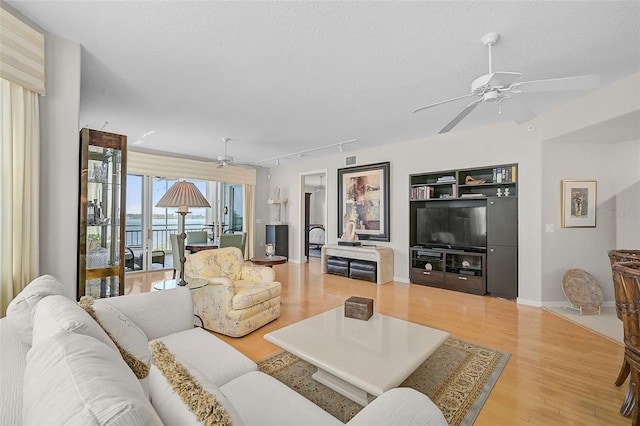 living room with a textured ceiling, rail lighting, light hardwood / wood-style floors, and ceiling fan