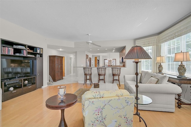 living room featuring a textured ceiling, ceiling fan, and light hardwood / wood-style flooring