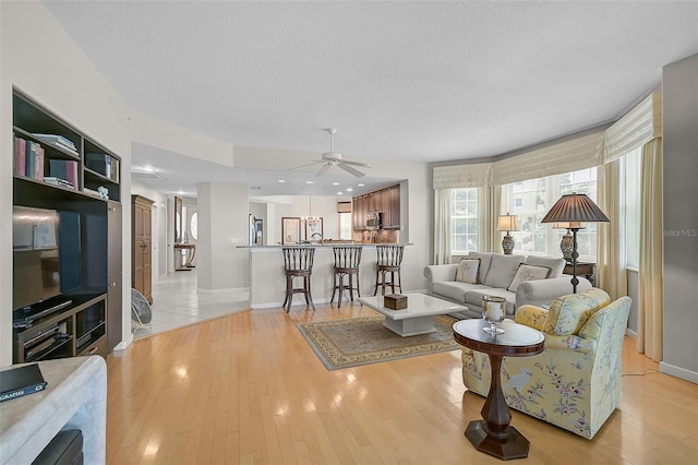 living room with light wood-type flooring, a textured ceiling, and ceiling fan