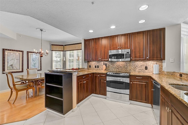 kitchen featuring an inviting chandelier, stainless steel appliances, kitchen peninsula, and a textured ceiling