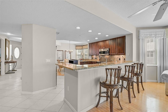 kitchen with ceiling fan with notable chandelier, kitchen peninsula, a breakfast bar area, light stone countertops, and a textured ceiling