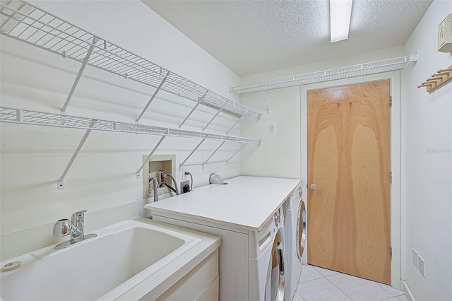 washroom featuring a textured ceiling, light tile patterned flooring, separate washer and dryer, and sink