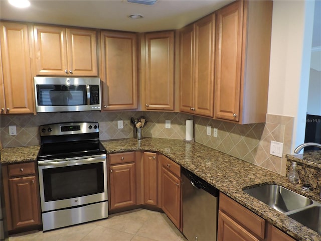 kitchen featuring sink, stainless steel appliances, backsplash, light tile patterned floors, and dark stone countertops