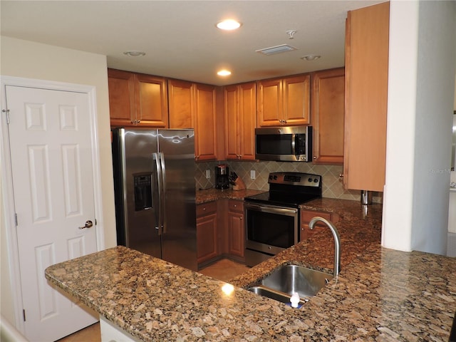 kitchen with sink, kitchen peninsula, backsplash, stone counters, and appliances with stainless steel finishes