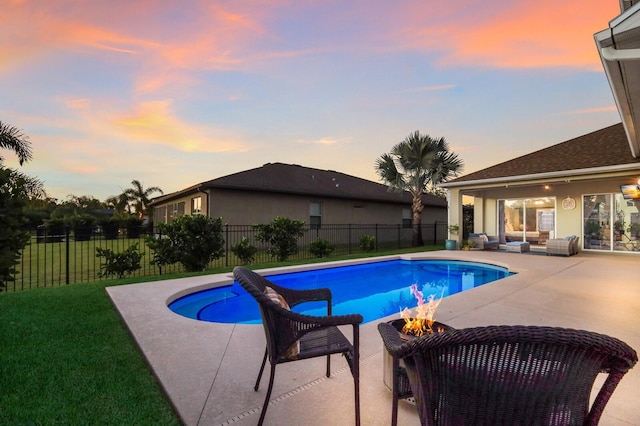 pool at dusk with a patio area, a fire pit, and a lawn