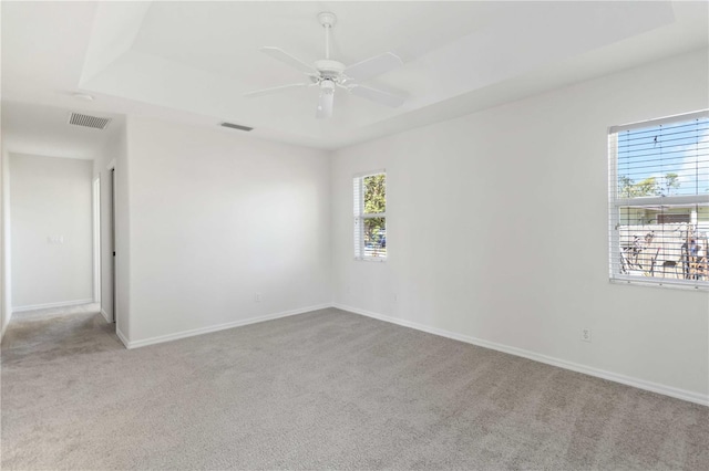 empty room with light carpet, a tray ceiling, and ceiling fan