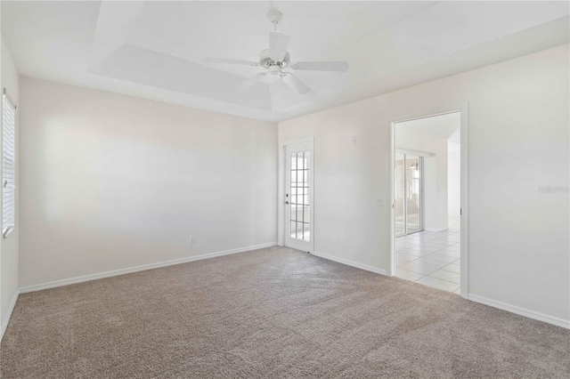 empty room with ceiling fan, a raised ceiling, and light carpet