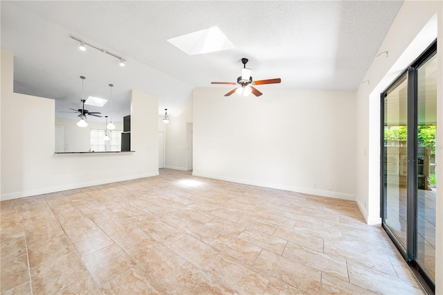 spare room with a textured ceiling, rail lighting, lofted ceiling with skylight, and ceiling fan