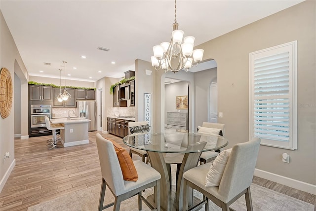 dining area featuring an inviting chandelier, sink, and light hardwood / wood-style flooring