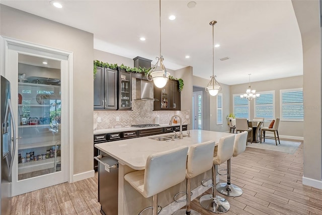 kitchen with light wood-type flooring, dark brown cabinets, pendant lighting, sink, and a kitchen island with sink