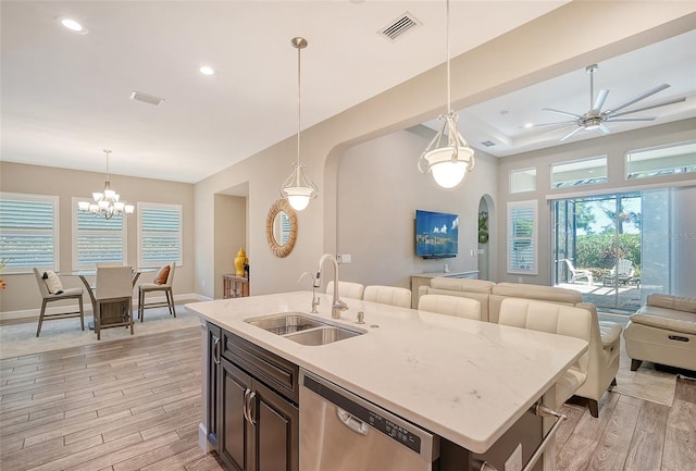 kitchen with sink, an island with sink, stainless steel dishwasher, pendant lighting, and light wood-type flooring