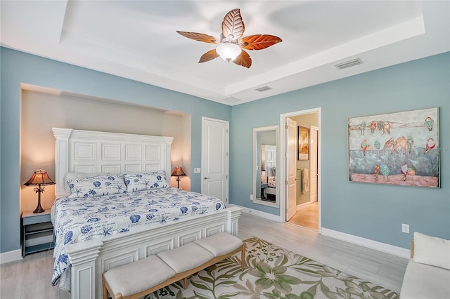 bedroom featuring light hardwood / wood-style floors, ceiling fan, connected bathroom, and a raised ceiling