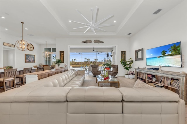 living room featuring ceiling fan with notable chandelier and a raised ceiling