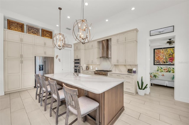 kitchen with a large island with sink, pendant lighting, sink, appliances with stainless steel finishes, and wall chimney exhaust hood