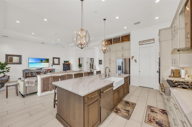 kitchen with ceiling fan, appliances with stainless steel finishes, a spacious island, decorative light fixtures, and sink