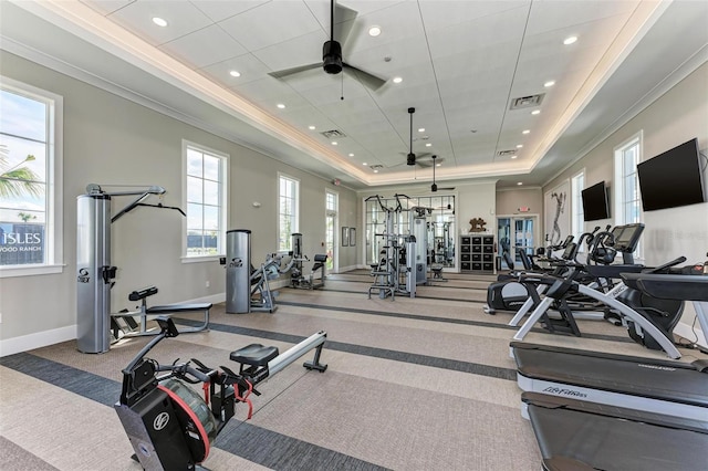 gym featuring a raised ceiling, ceiling fan, and ornamental molding