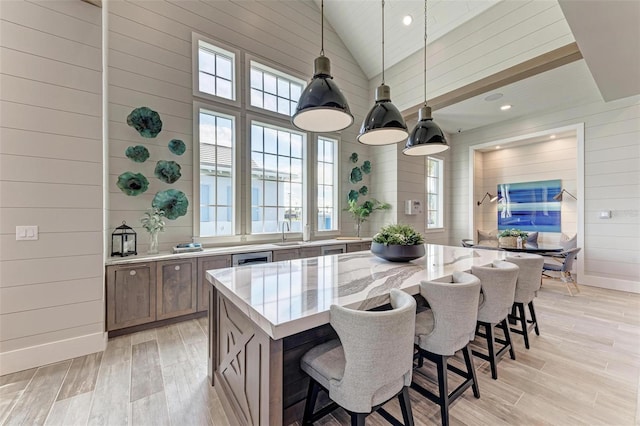 kitchen with wood walls, pendant lighting, a kitchen island, high vaulted ceiling, and light stone counters