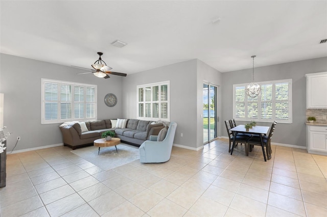 tiled living room with ceiling fan with notable chandelier