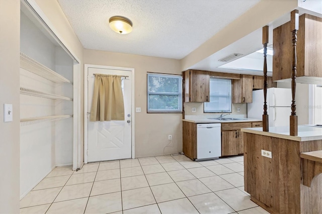 kitchen with a textured ceiling, sink, light tile patterned floors, and white appliances