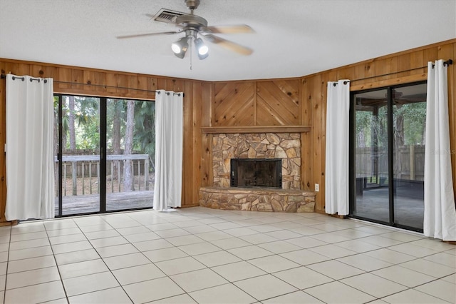 unfurnished living room with a textured ceiling, a fireplace, wooden walls, and ceiling fan