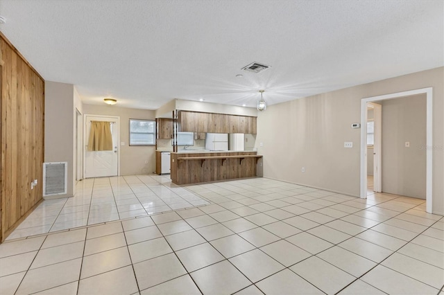 unfurnished living room with a textured ceiling, light tile patterned flooring, and wooden walls