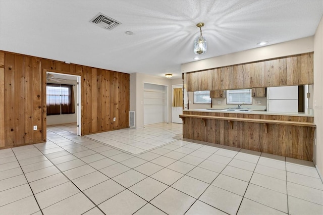 kitchen with kitchen peninsula, hanging light fixtures, white fridge, wooden walls, and light tile patterned floors